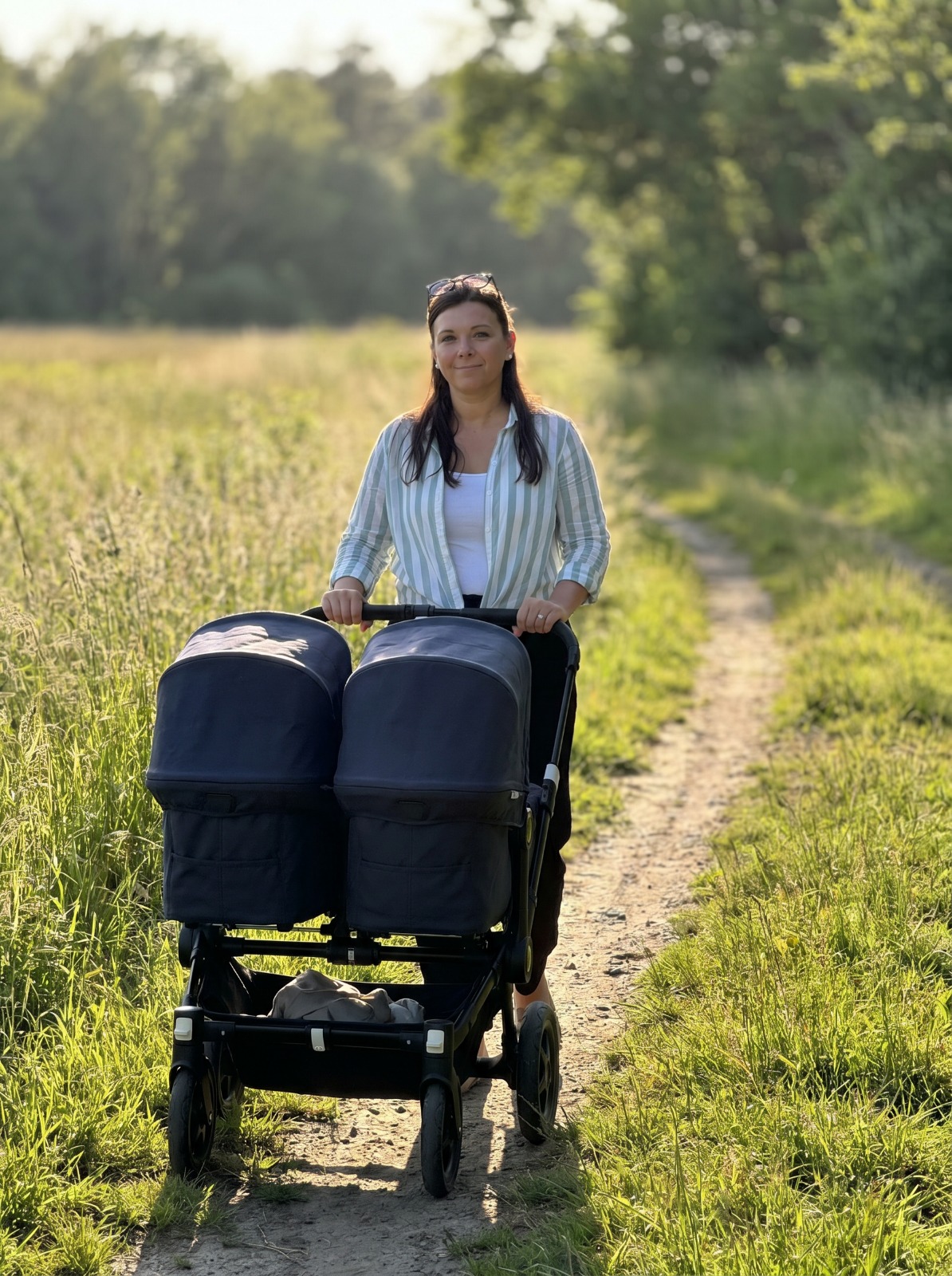 Mutter mit Zwillingskinderwagen auf einem sonnigen Feldweg